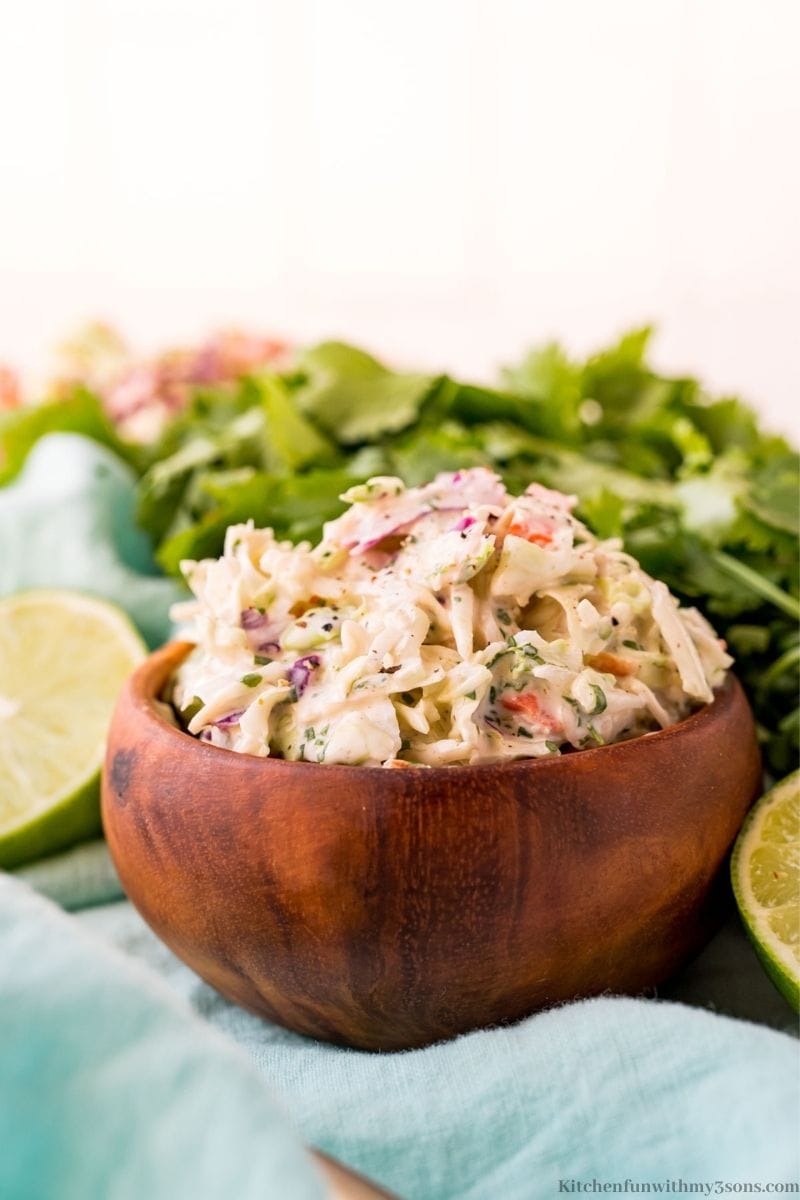 The slaw in a wooden bowl on a light blue cloth.