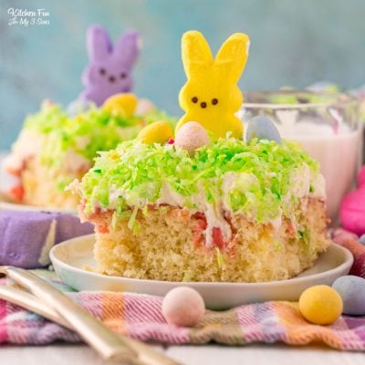 A yellow Peeps bunny perched on top of a decorated slice of Peeps Poke Cake.