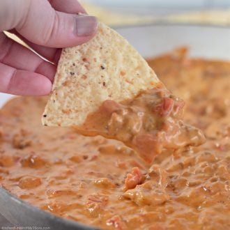 A hand dips a tortilla chip into a saucepan of rotel dip.