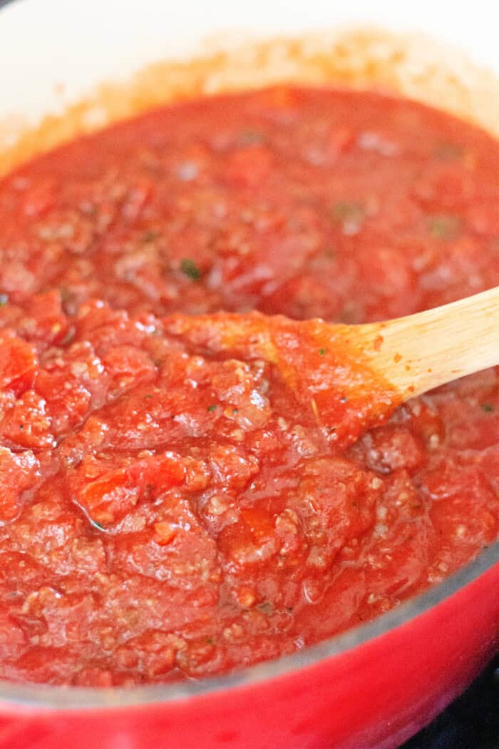 Italian sausage and ground beef are simmered with crushed and fire roasted tomatoes to make this the BEST Spaghetti Meat Sauce recipe. A wooden spoon stirring spaghetti meat sauce