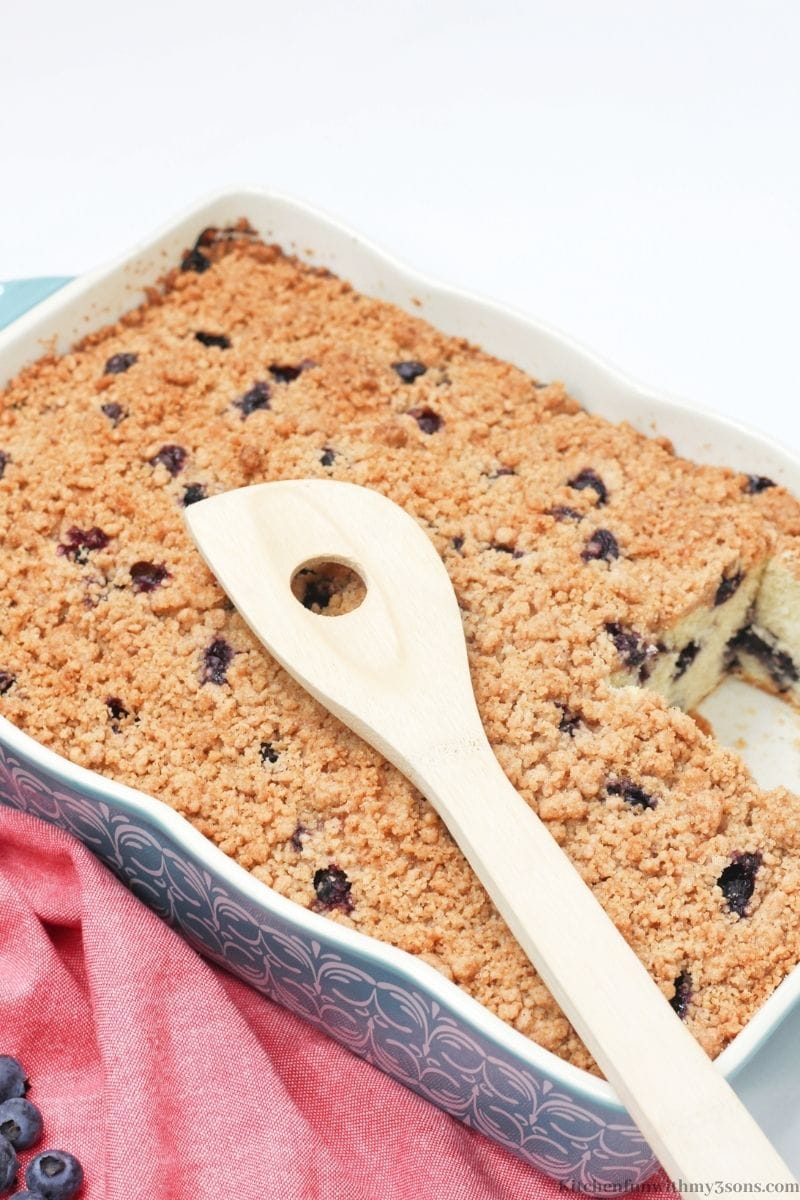 The crumble cake with a slice taken out with a wooden spoon on top.