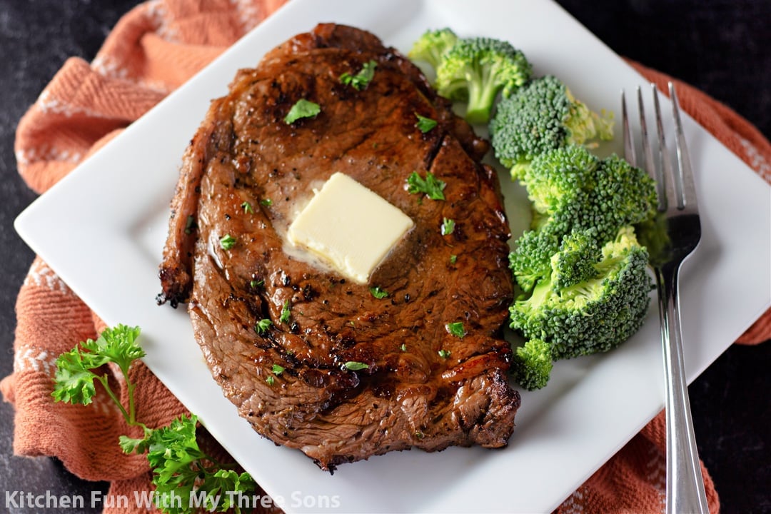 A steak and broccoli on a white plate with a brown napkin.