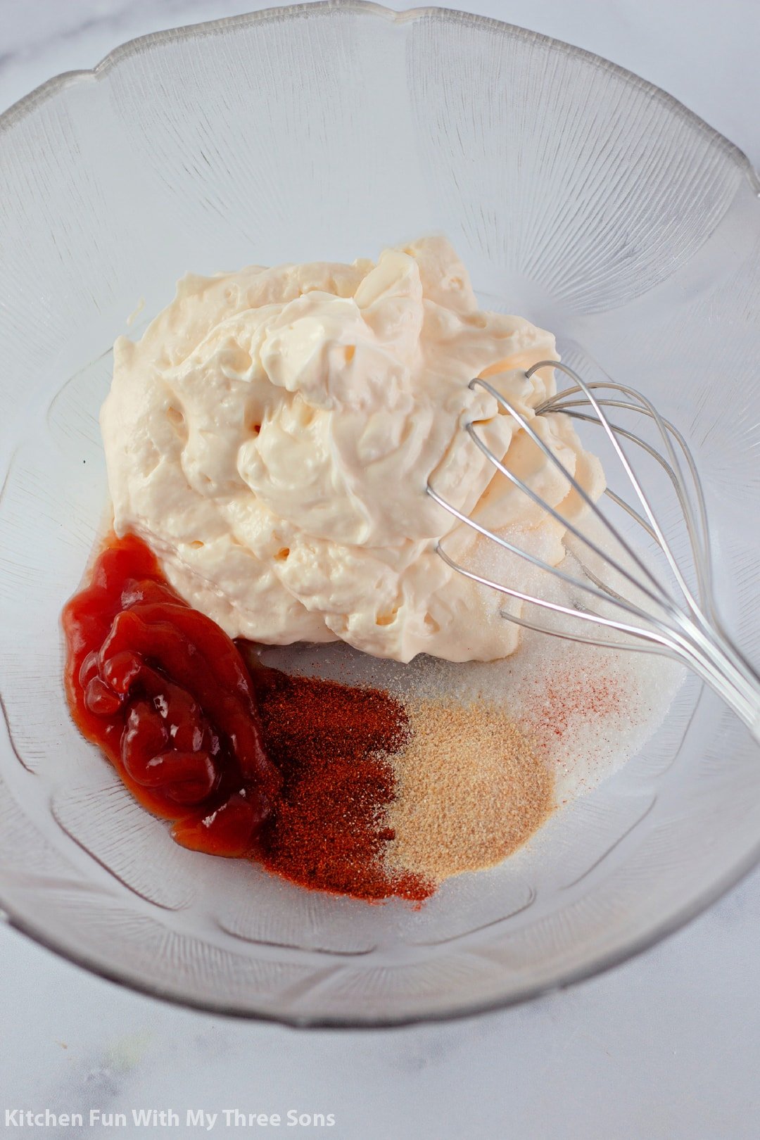 whisking together mayonnaise, ketchup, sugar, and spices in a clear bowl.