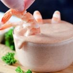 A shrimp is dipped into a bowl of yum yum sauce.