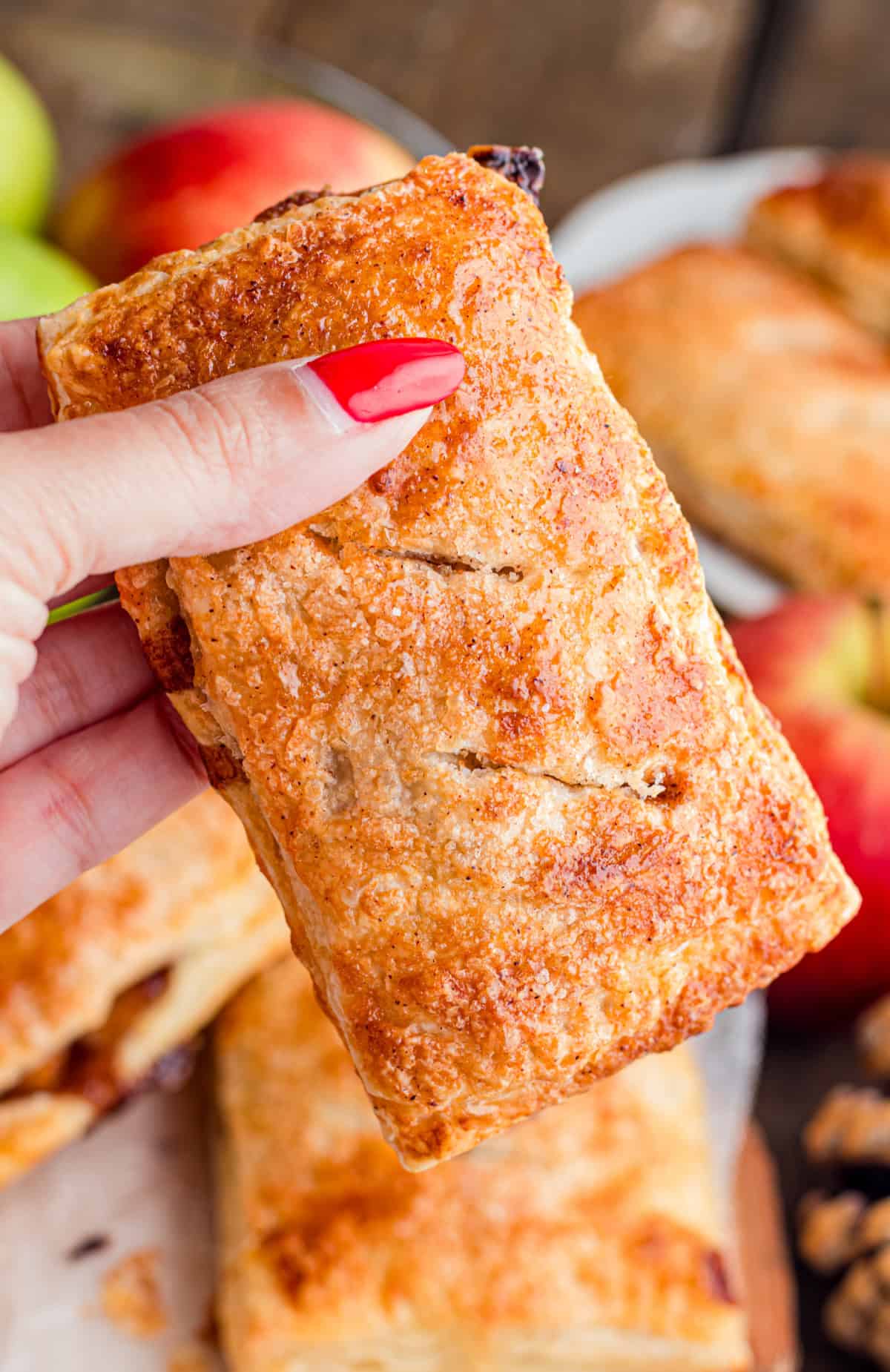 These Apple Hand Pies are filled with gooey apple pie filling wrapped in flaky puff pastry and baked until deeply golden and crisp. Hand holding an apple hand pie.