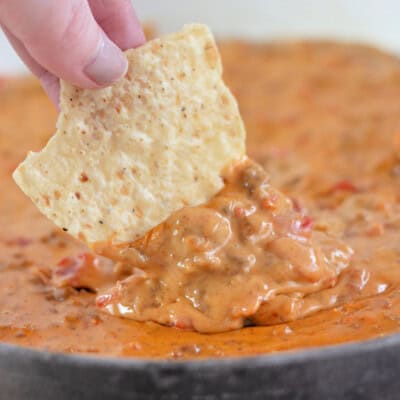 A tortilla chip being dipped into Rotel Dip.