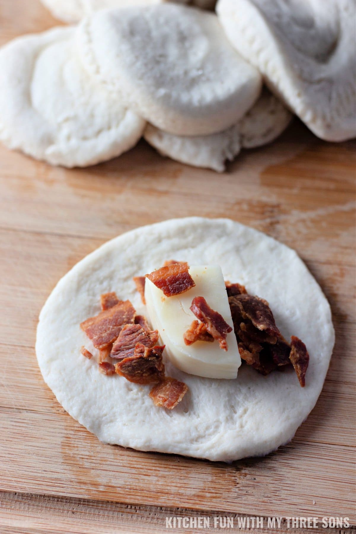 A small disc of biscuit dough topped with a piece of mozzarella cheese and crumbled bacon.