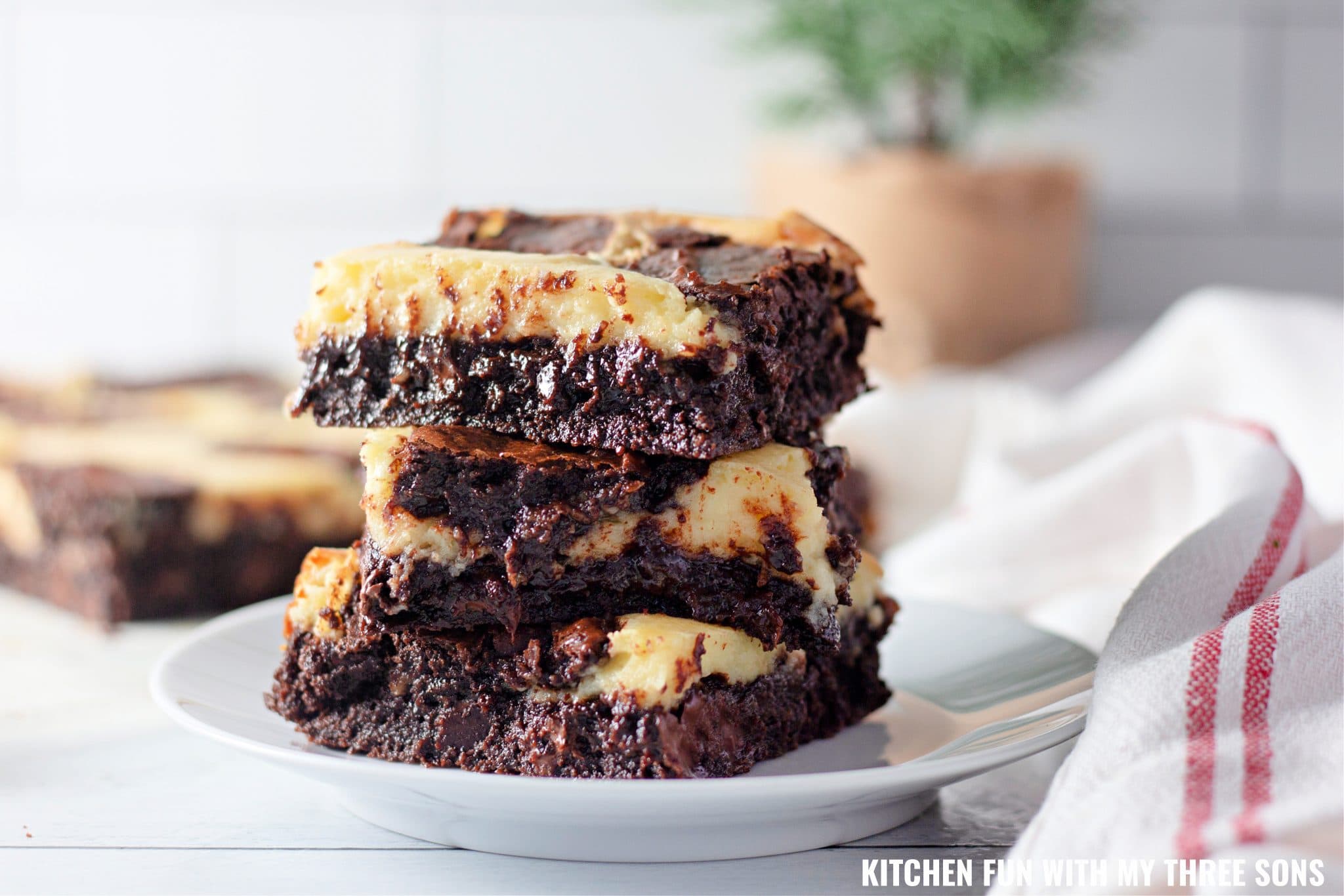 Three cheesecake brownies stacked on a white plate.