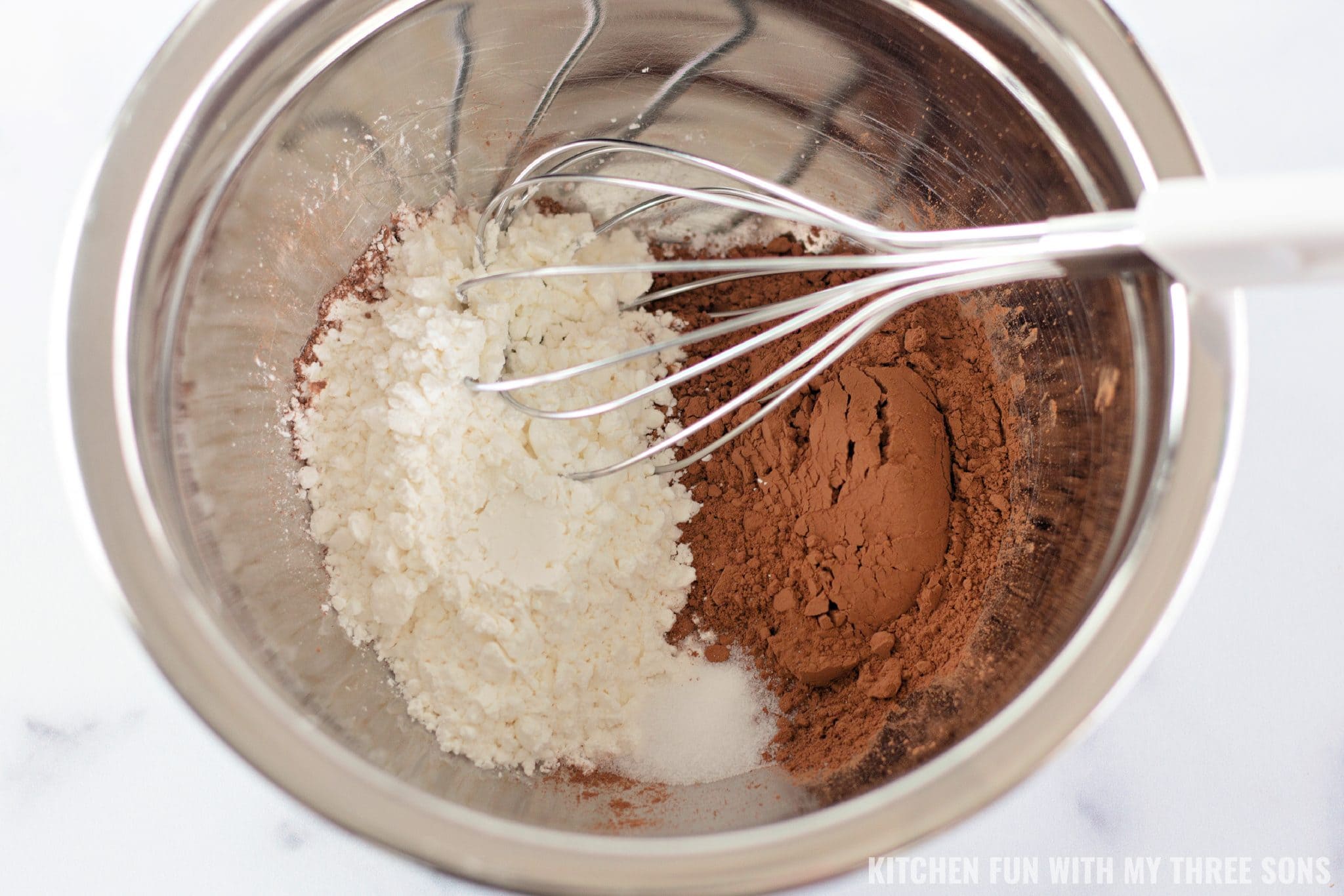 Dry brownie ingredients combined in a metal bowl with a whisk.