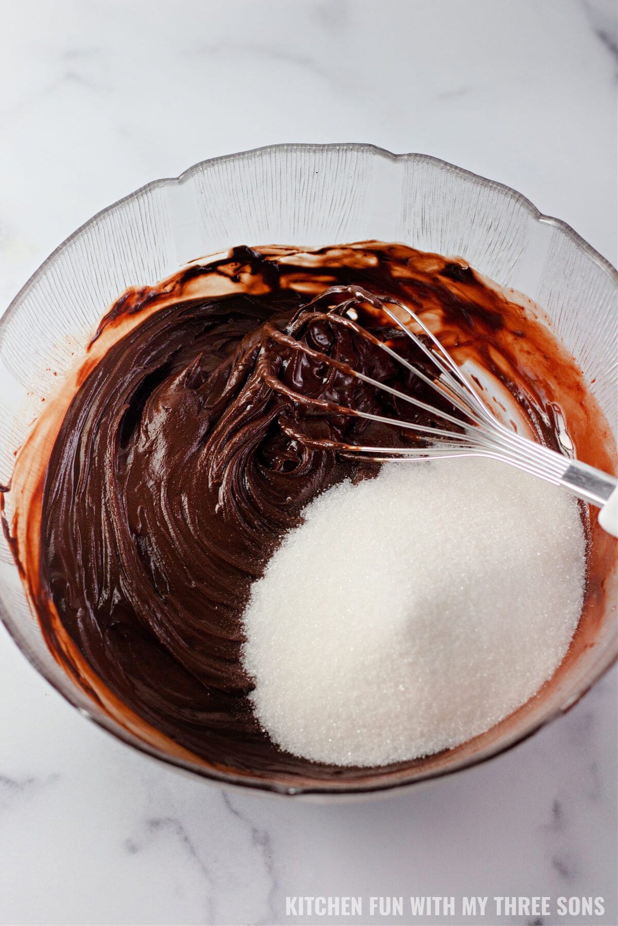 Sugar added to brownie batter in a glass bowl.