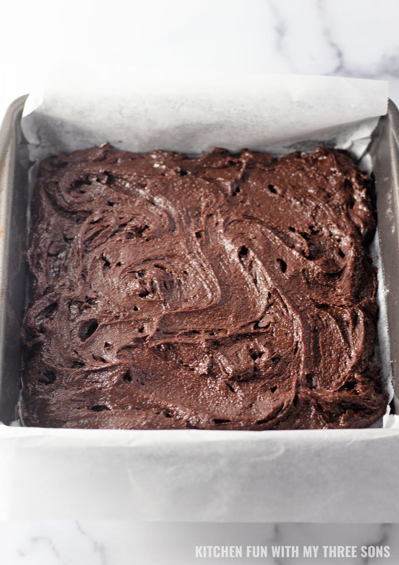 Brownie batter spread into a lined baking pan.