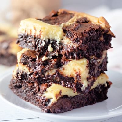 Three cheesecake brownies stacked on a white plate.
