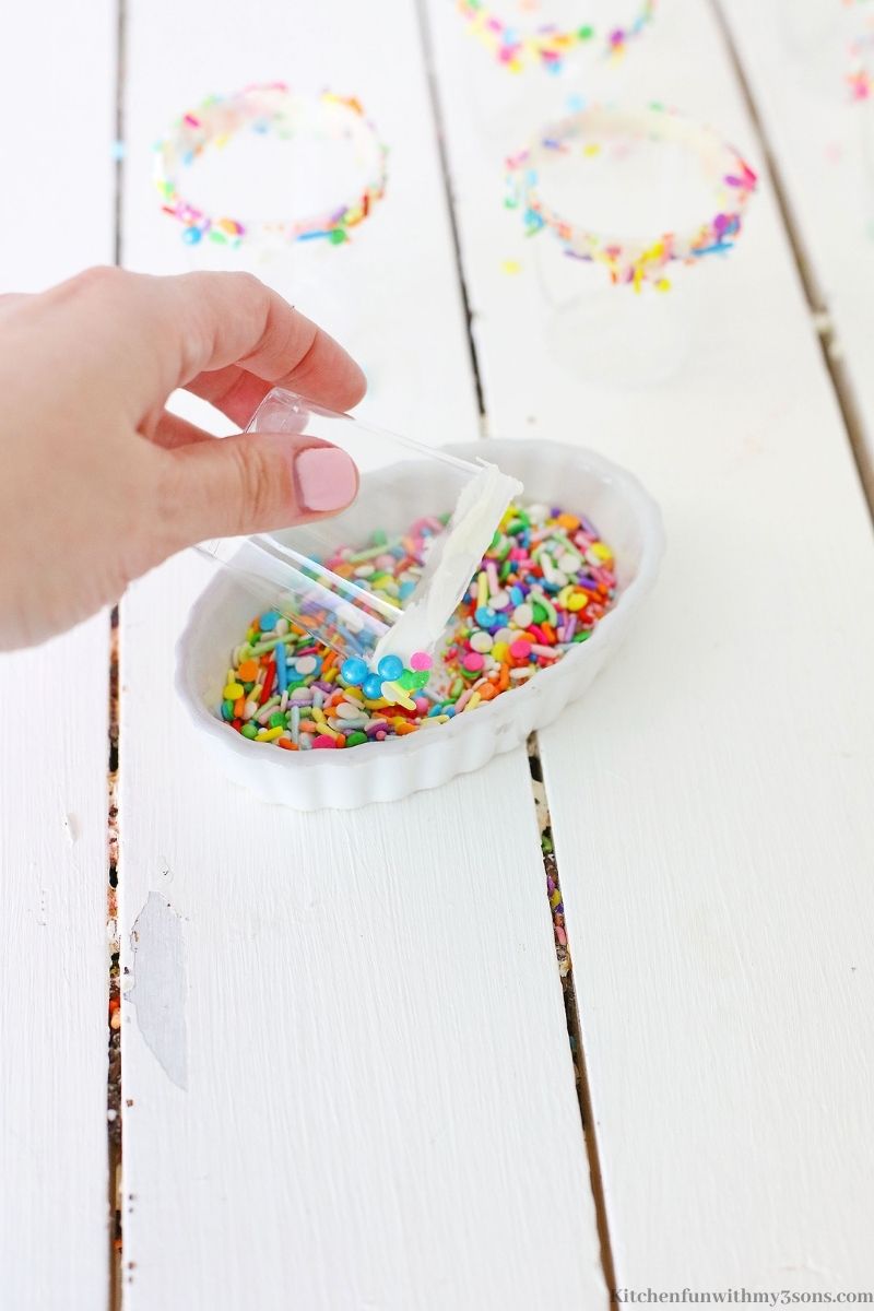 Dipping the rim of the shot glass in sprinkles.