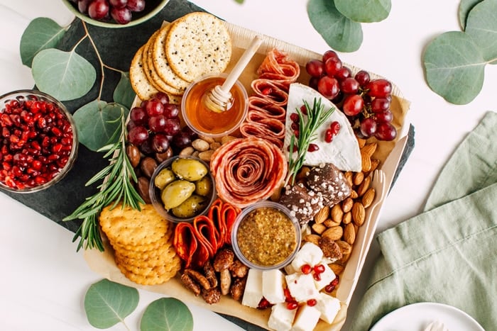 Overhead view of a charcuterie board with salami, grapes, crackers, honey, and other ingredients