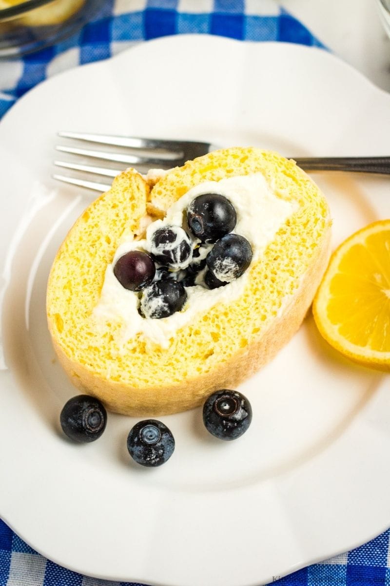 A slice of the cake on a serving plate with a lemon slice and more blueberries.