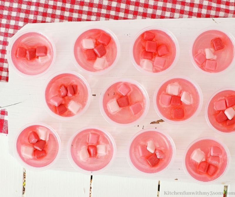 All the jello shots on a white board on a red cloth.