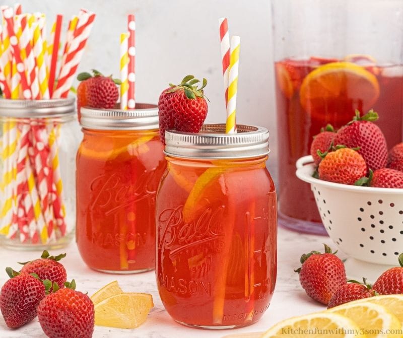 two mason jars with the tea inside with straws and garnished with a whole strawberry.