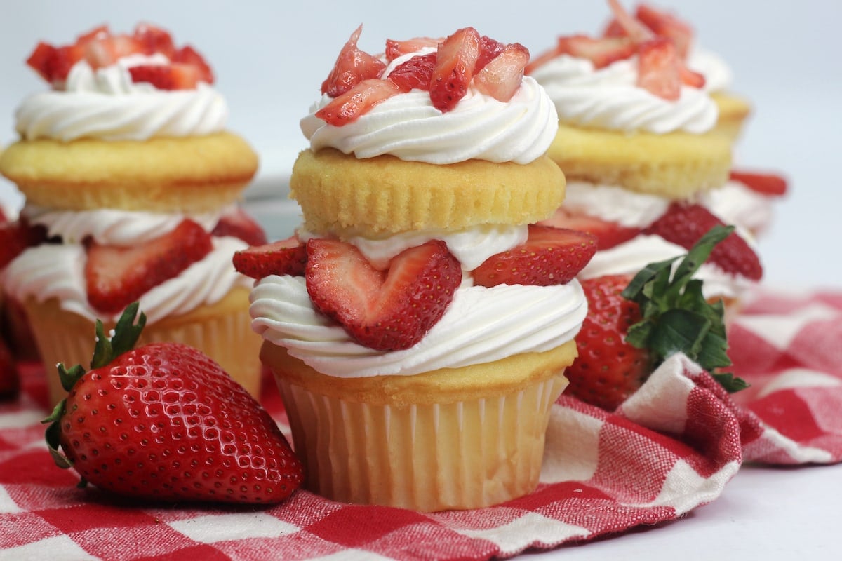 A strawberry shortcake cupcake on a red checkered tablecloth