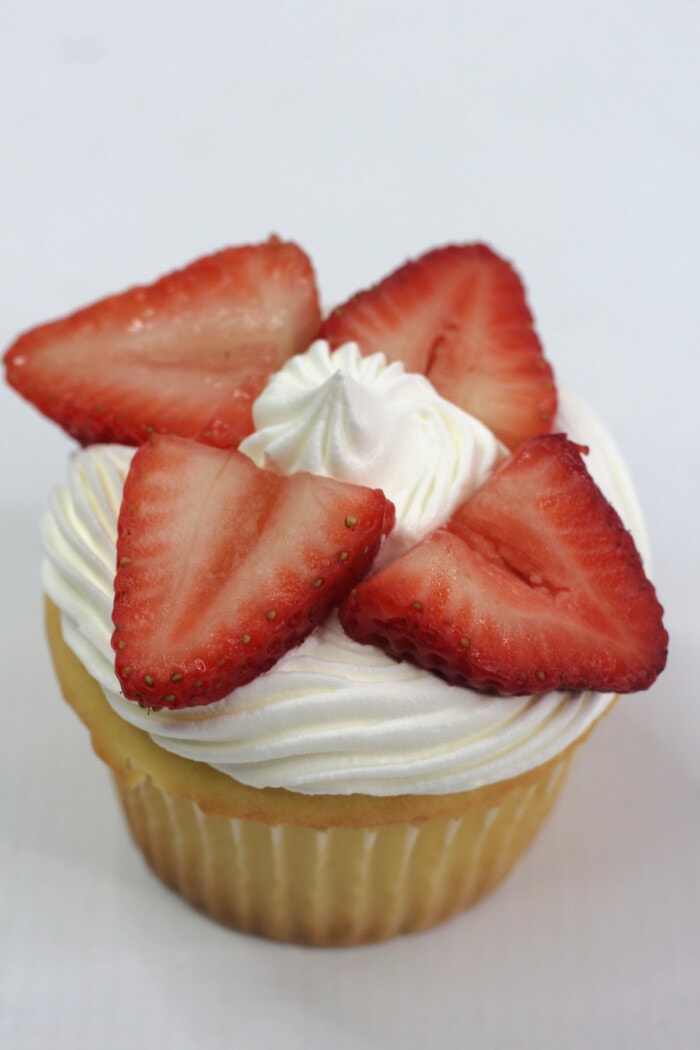 A cupcake topped with whipped cream and sliced strawberries