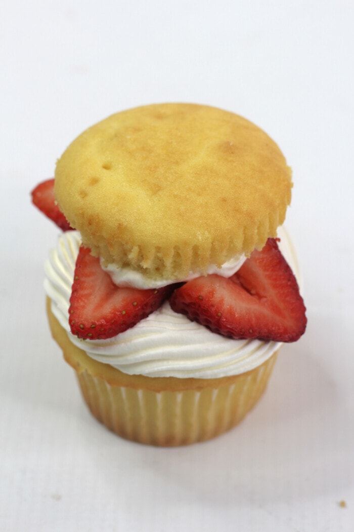 A cupcake topped with whipped cream, strawberries, and a cupcake top