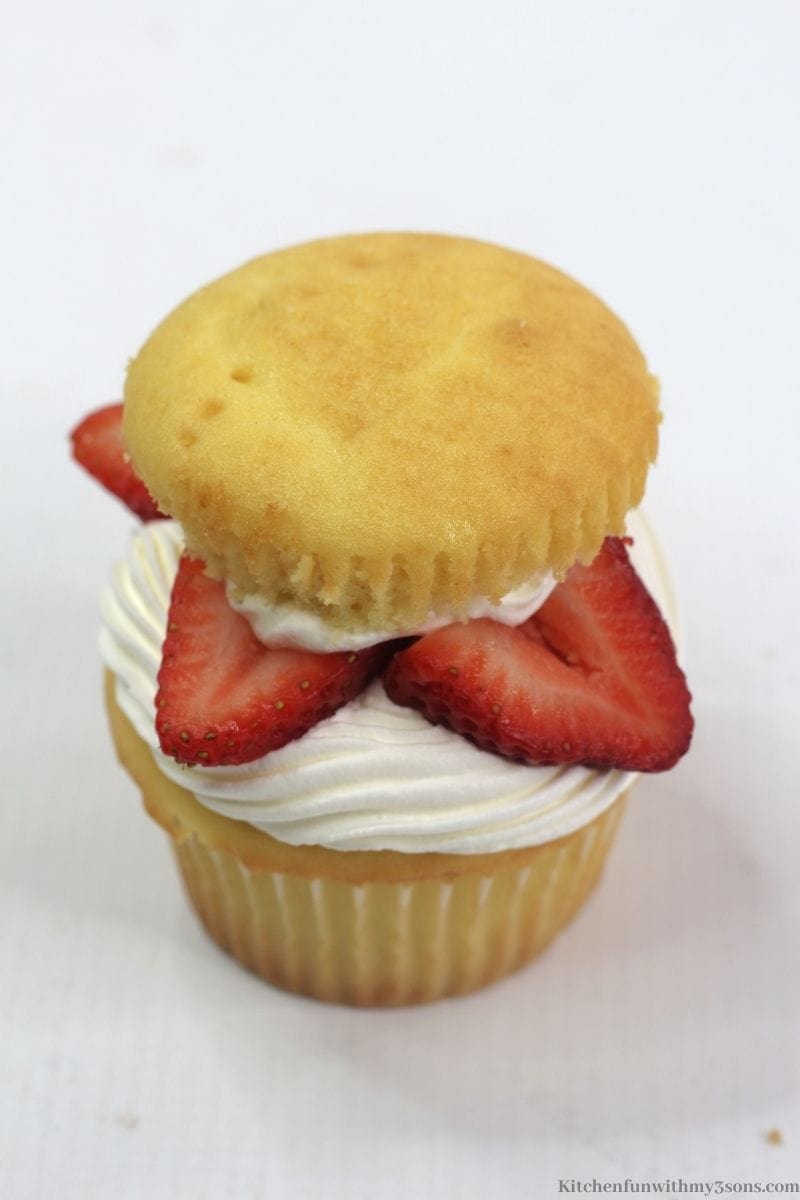 The top of the cupcake placed on top of the whipped cream and strawberries.
