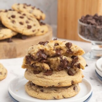 Four chocolate chip cookies stacked on a white plate, with the top two cookies broken in half.