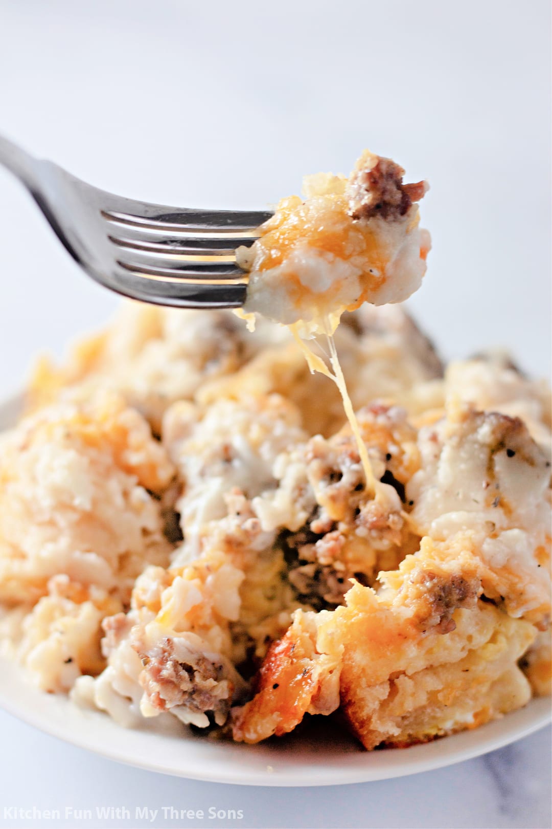 A forkful of biscuits and gravy held over a casserole serving on a plate.