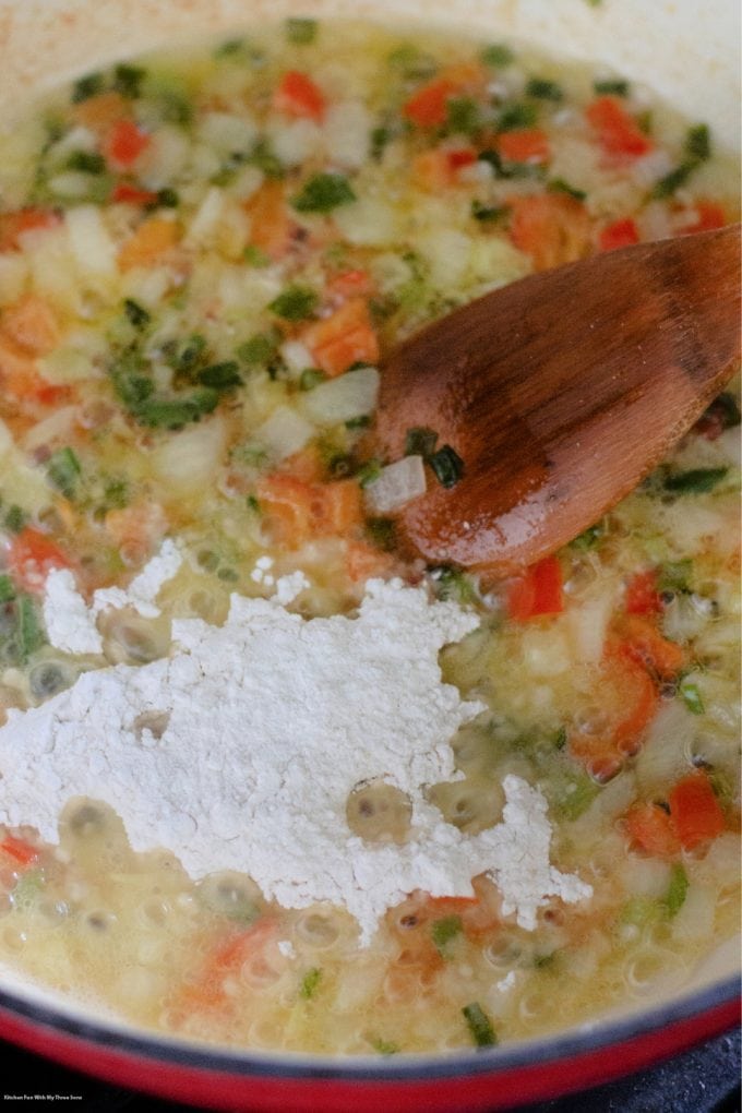 adding flour to the cooking vegetables in the pot.