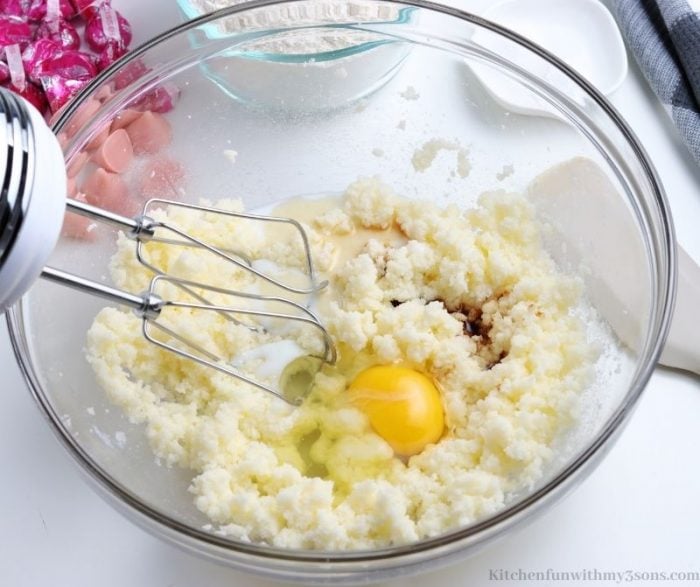 Egg and vanilla added to a bowl of wet cookie batter ingredients, with a hand mixer.