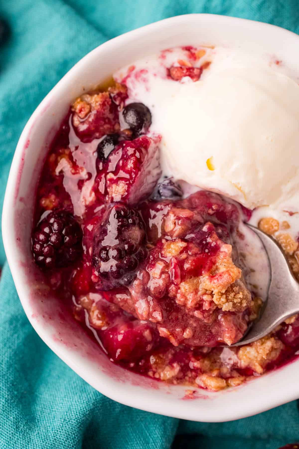 Berry Crisp topped with vanilla ice cream in a bowl with a spoon