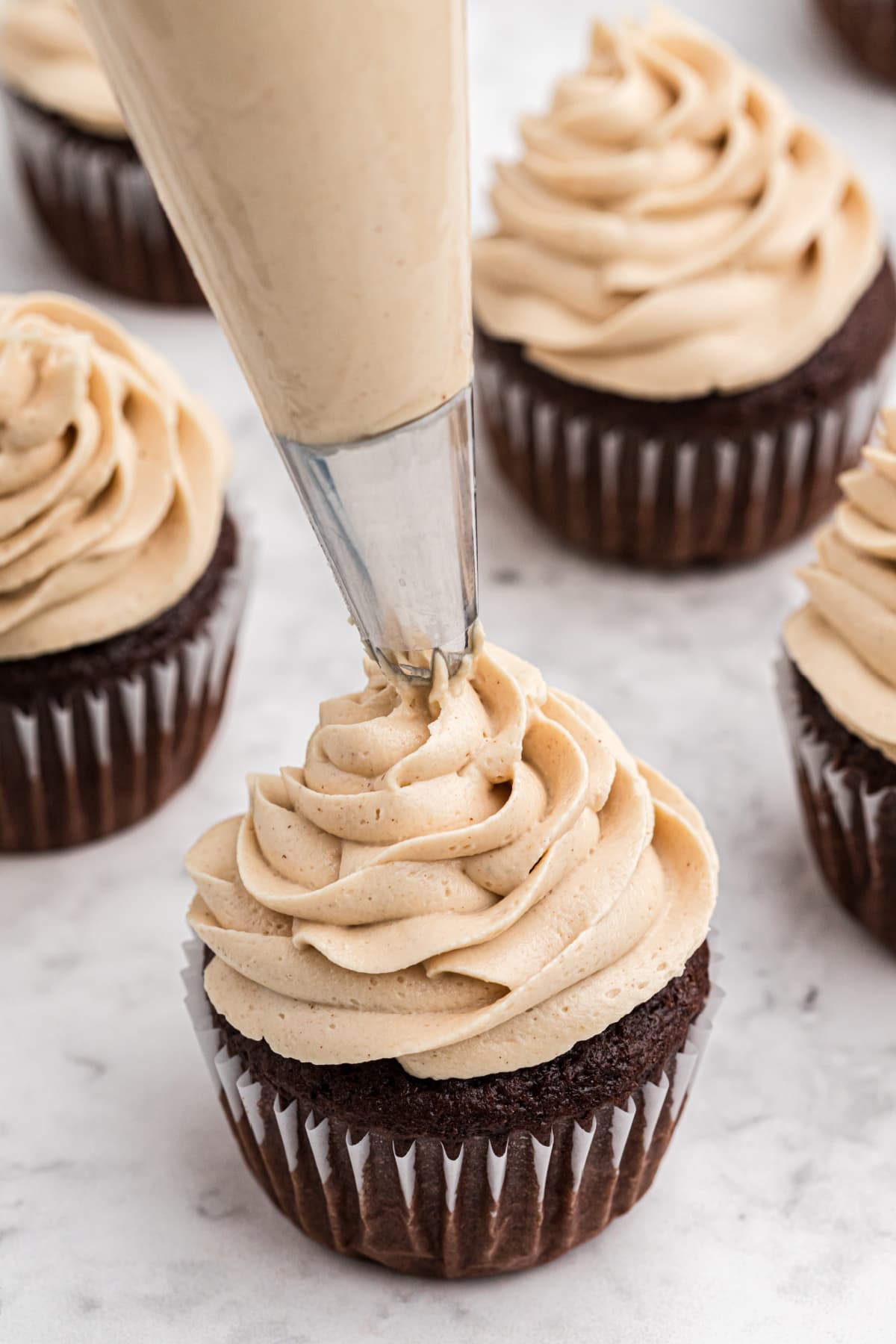 Piping peanut butter frosting on a chocolate cupcake