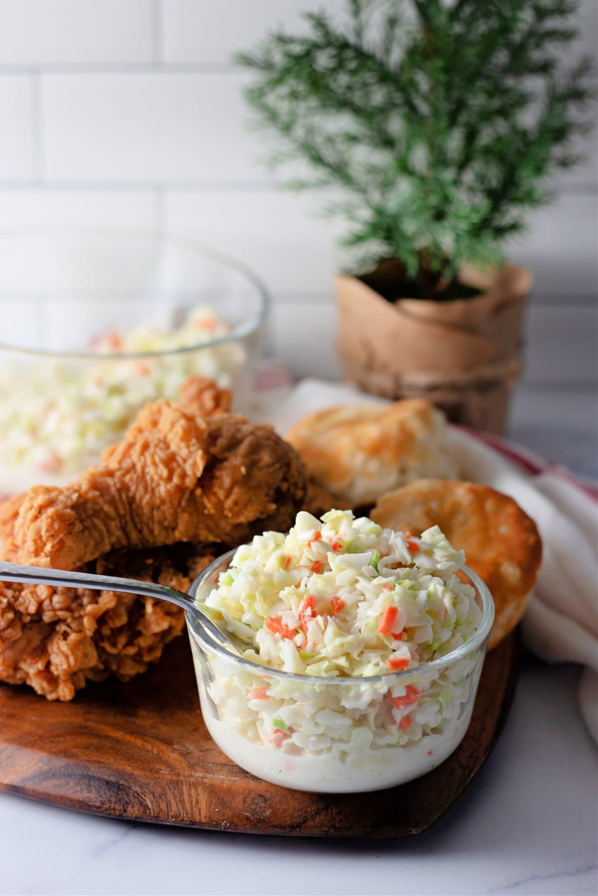A spoon mixing a small dish of KFC coleslaw in front of fried chicken and biscuits
