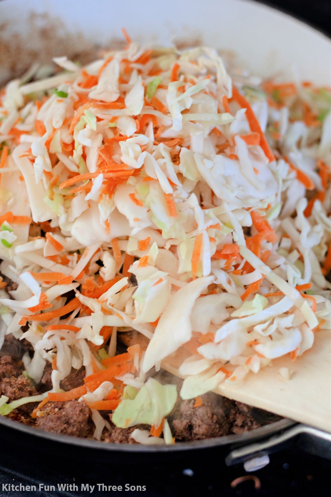 Creamy coleslaw being added to a pan of ground beef