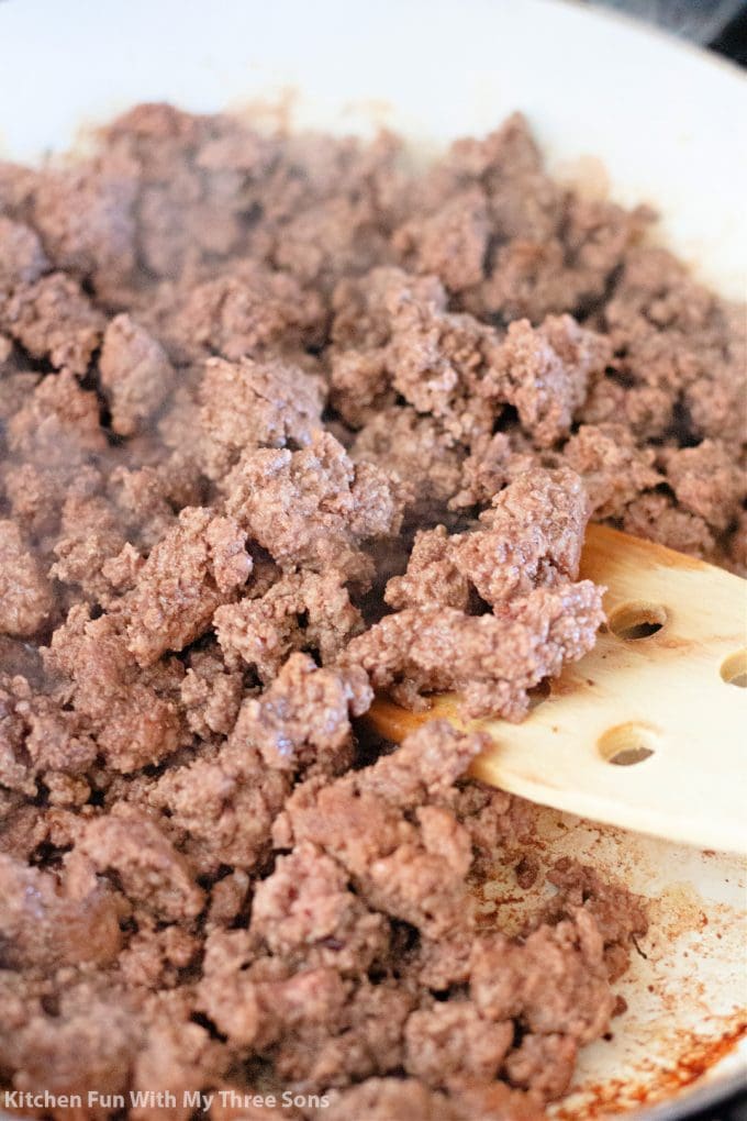 ground beef in a pan with a wooden spoon.