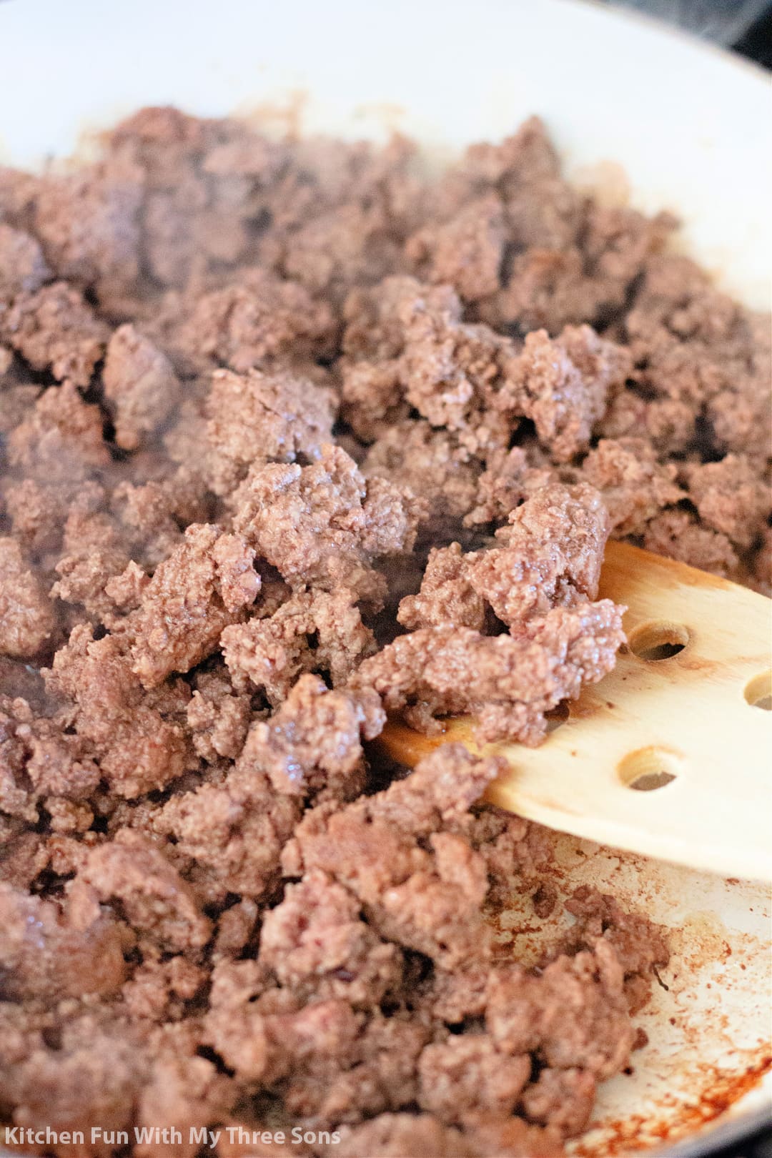A pan full of ground beef being stirred with a wooden spatula