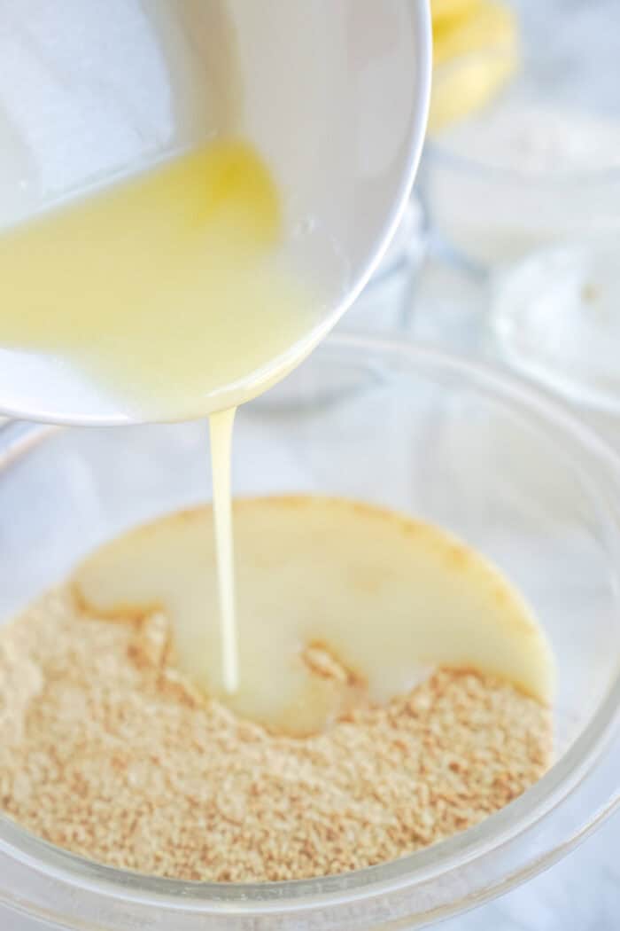 pouring melted butter over crushed graham crackers

