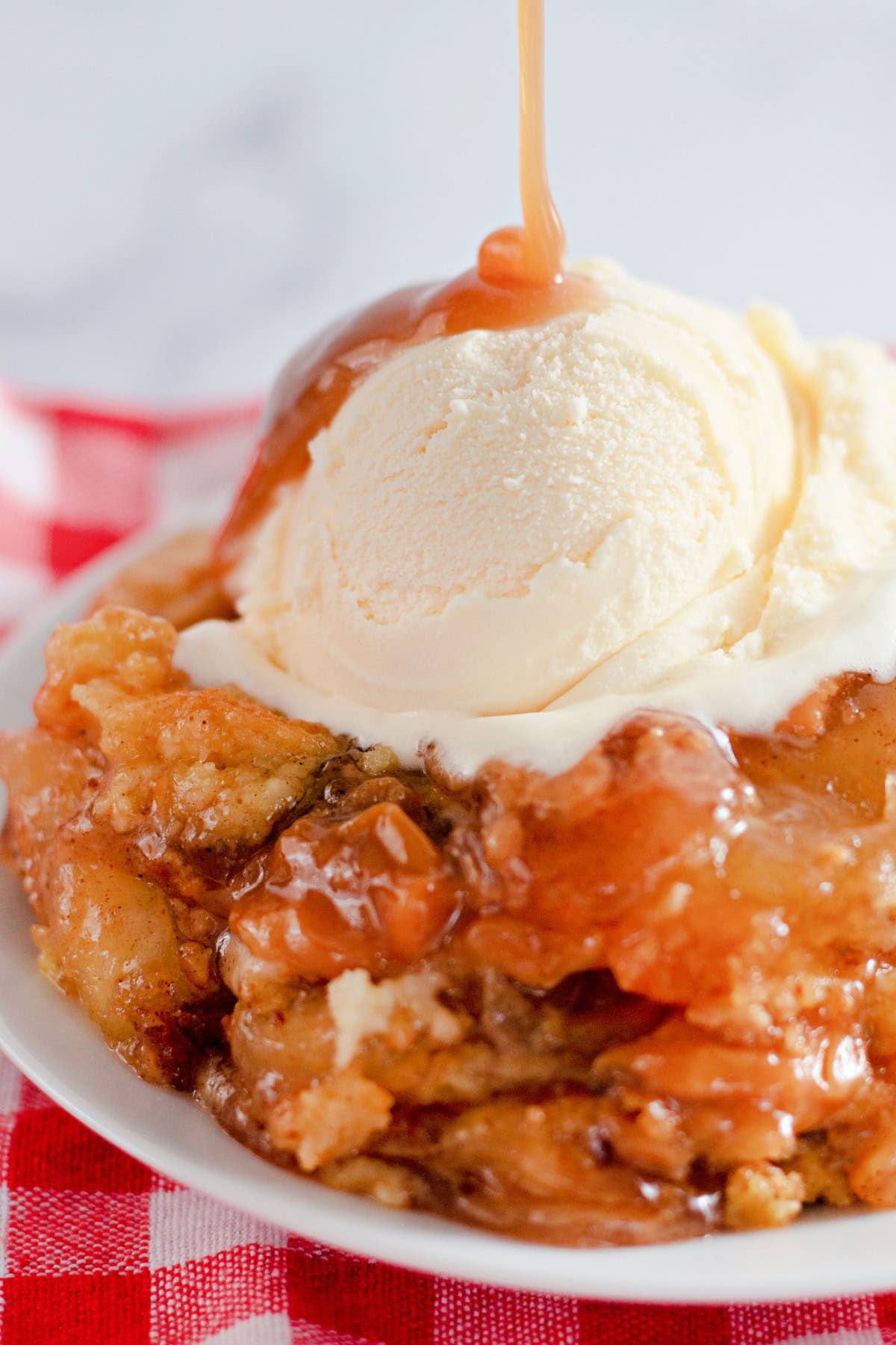 Pouring Caramel over caramel apple dump cake with ice cream