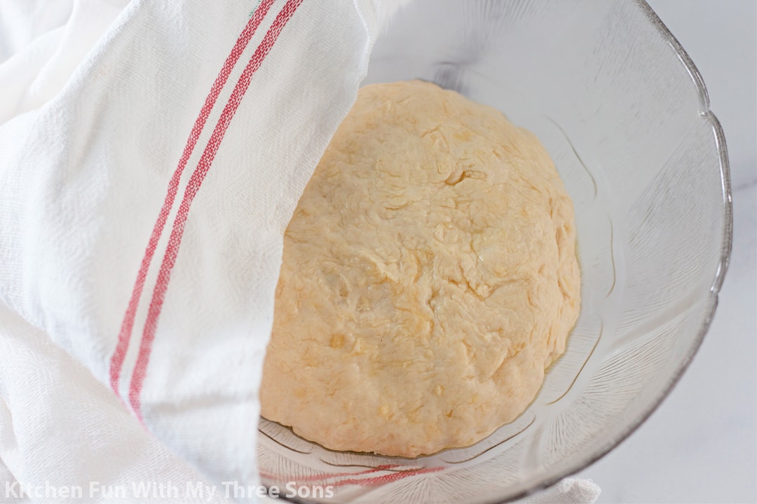 allowing the dough to rest and rise in a bowl covered with a kitchen towel.