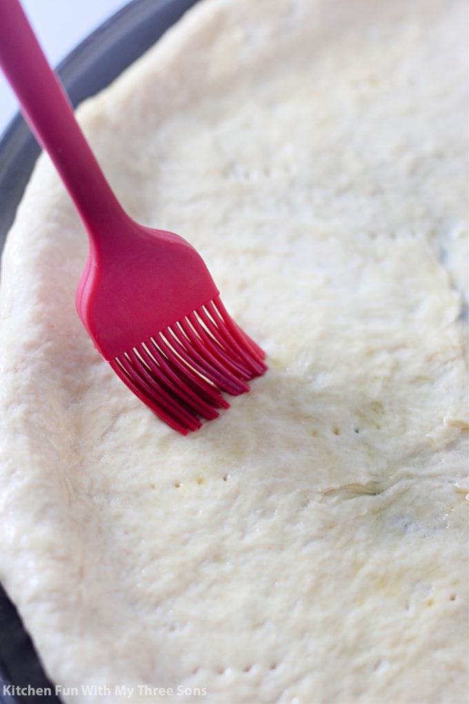 brushing pizza dough with olive oil.