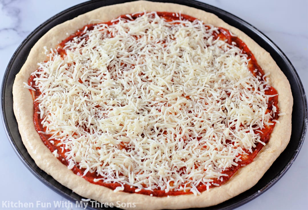 topping the pizza with shredded mozzarella cheese.