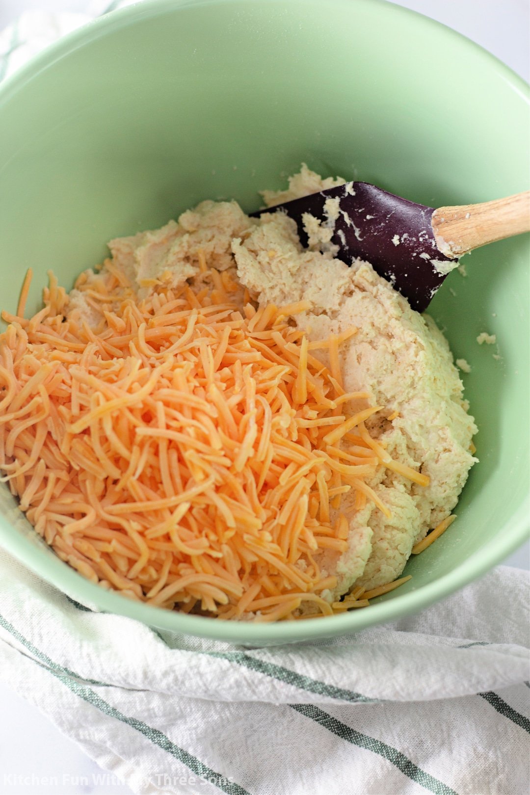 Shredded cheddar cheese added to a mixing bowl of biscuit dough.