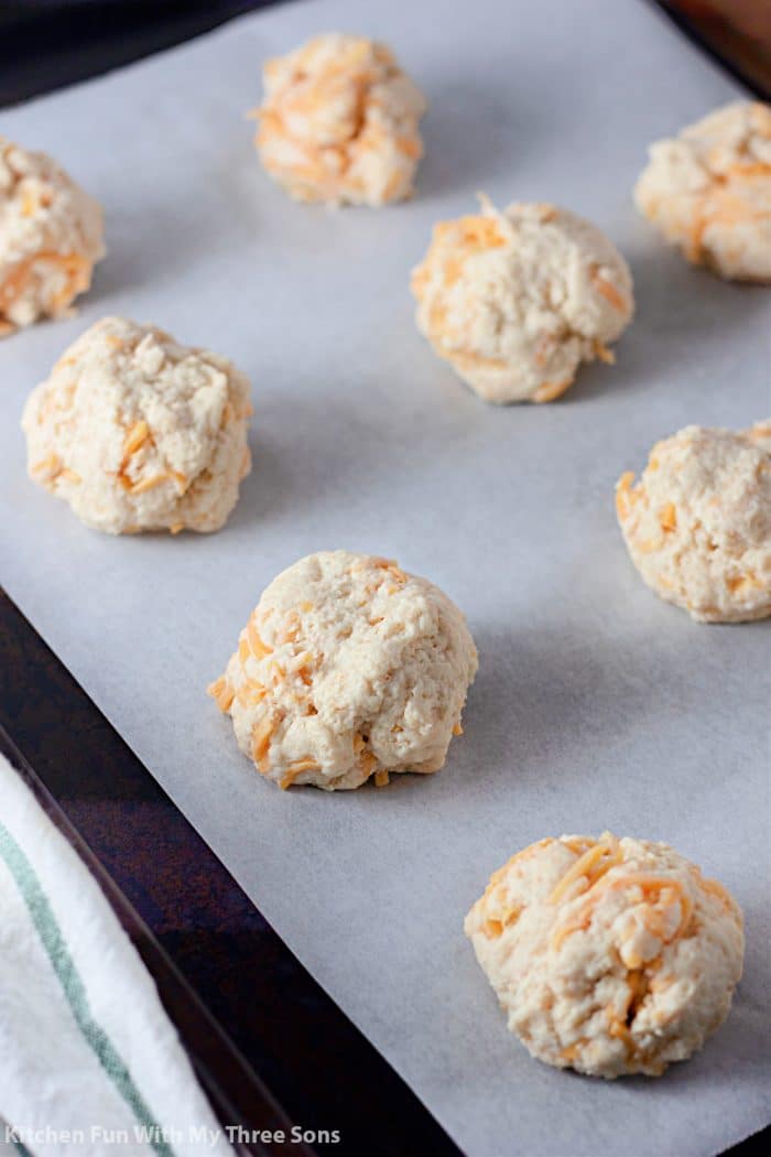 Unbaked cheddar biscuit dough balls on a lined baking sheet.