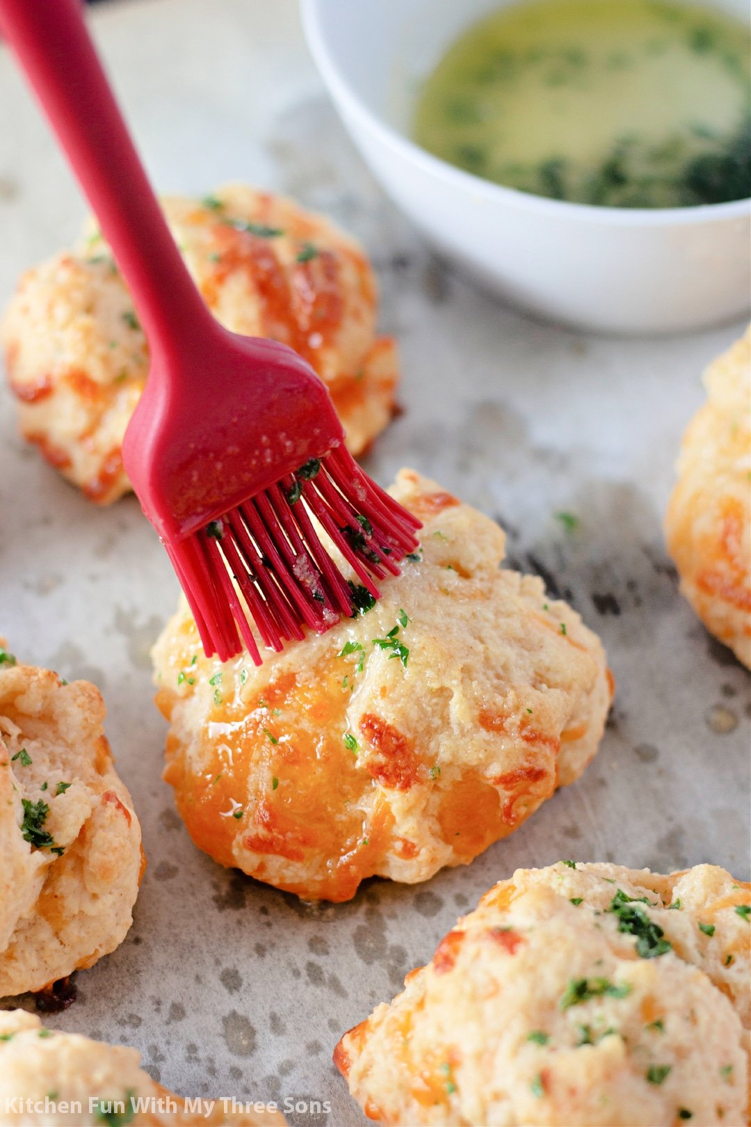 A rubber basting brush coats the tops of Cheddar Bay Biscuits with garlic butter.