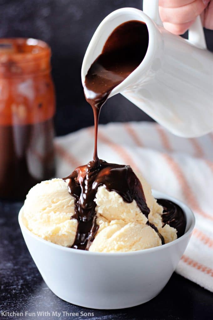 pouring hot fudge over vanilla ice cream in a white bowl.