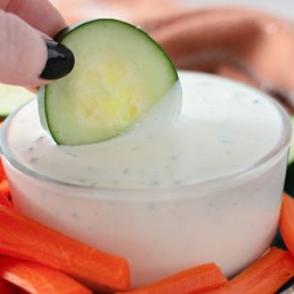 A cucumber being dipped into homemade ranch dressing