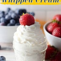 Homemade whipped cream in a glass jar with a strawberry on top.