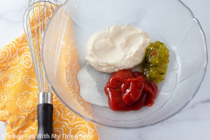 mayonnaise, ketchup, sugar, vinegar, and relish in a clear bowl with a whisk.