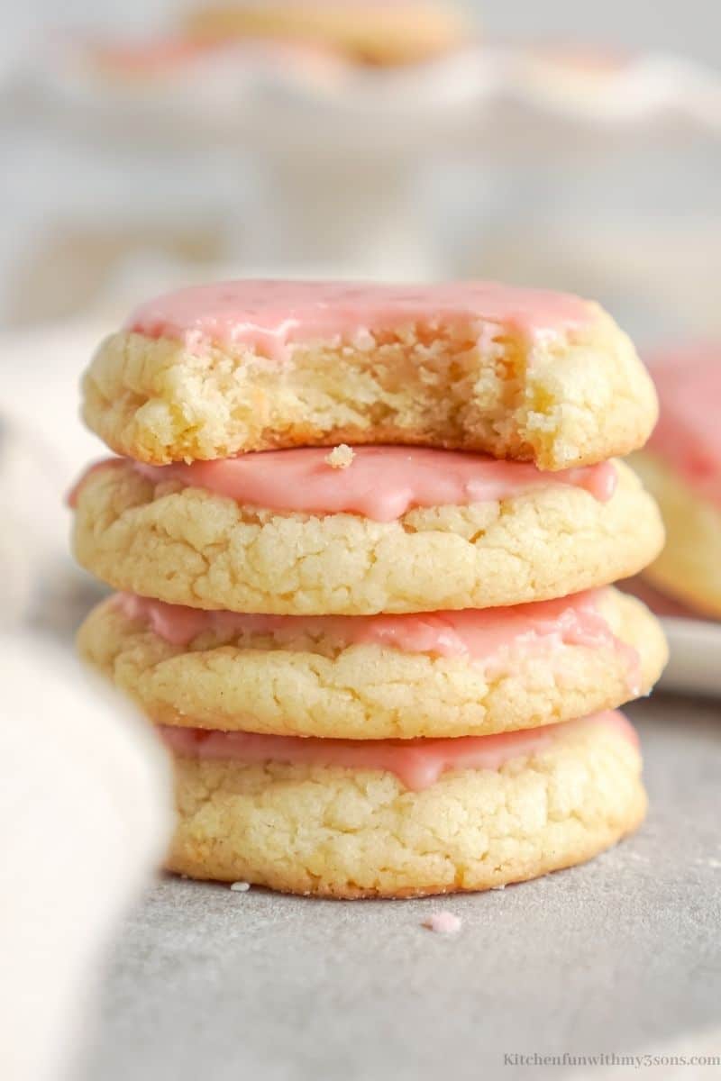Four strawberry sugar cookies stacked on top of each other, with a bite missing from the top cookie.