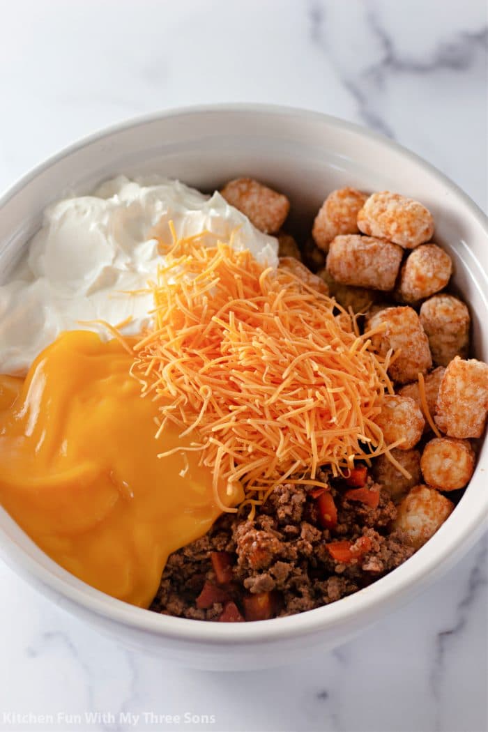 A white bowl filled with cooked beef, cheese and tater tots