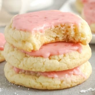 Three strawberry sugar cookies stacked, with a bite missing from the top cookie.